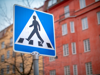 Blue road crossing sign with red building in the background in Stockholm