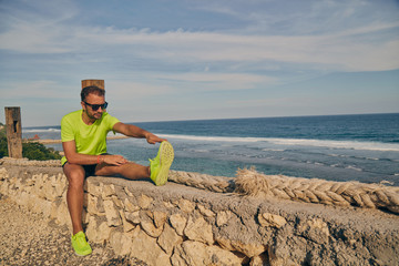Naklejka na ściany i meble Sportsman stretching on a tropical exotic cliff near the ocean.