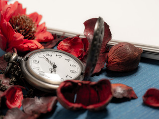 golden pocket watch put on dried leaves and blank notebook on wooden retro black table. Copy space for text and content.
