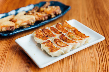 Yaki-Gyoza set (Japanese Pan-Fried Dumplings) served on white plate with fried chicken in background.