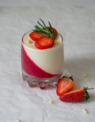 Panna cotta dessert with strawberry jelly and vanilla mousse in a glass beaker, decorated with fresh strawberries and rosemary, on a white background. Holiday food concept. Selective focus.
