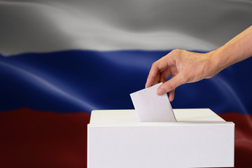 Close-up of human hand casting and inserting a vote and choosing and making a decision what he wants in polling box with Russia flag blended in background.