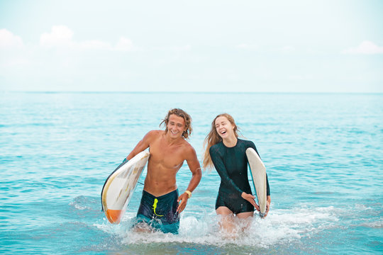 Surfers at the beach- Smiling couple of surfers walking on the beach and having fun in summer. Extreme sport and vacation concept