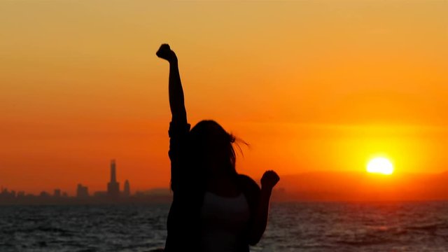 Silhouette of an excited woman jumping at sunset celebrating success on the beach
