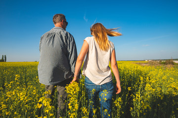 Romantic couple is walking through the field of yellow flowers