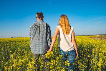 Fototapeta premium Romantic couple is walking through the field of yellow flowers