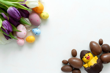 Tulips, chocolate Easter eggs and duck on white wooden background. Flat lay. Top view.