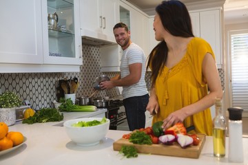 Woman cutting vegetables while man cooking food in kitchen