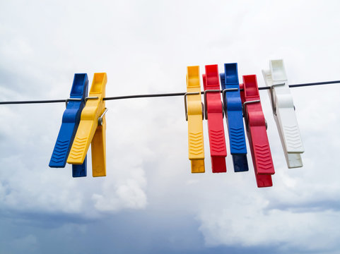  Pinzas de colores agarradas a la cuerda  de tender la ropa a secar, con fondo de cielo nublado