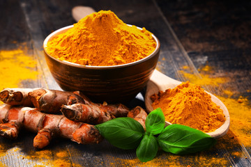 Composition with bowl of turmeric powder on wooden table