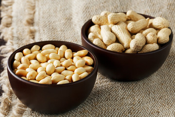 Peanuts in the shell and peeled close-up in cups. Roasted peanuts in their shells and peeled against a brown cloth.