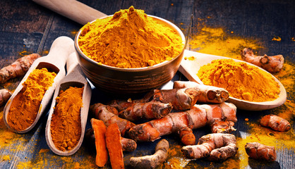 Composition with bowl of turmeric powder on wooden table