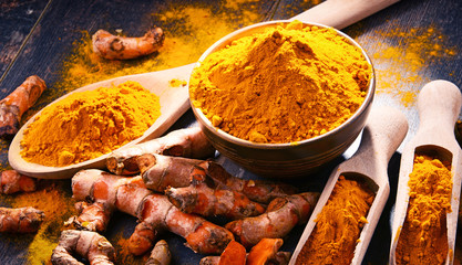 Composition with bowl of turmeric powder on wooden table