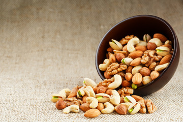 Walnut platter spilled out of the cup on the background of cloth from burlap. Nuts as structure and background, macro.