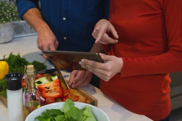 Couple cutting vegetables while using digital tablet in kitchen