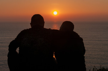Sunset in front of the sea in golden hour with silhouette of couple of friends