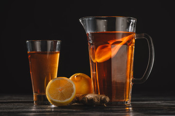 tea with lemons and ginger root in glass and jar on wooden table isolated on black