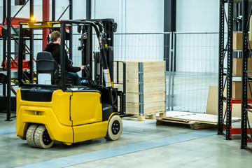 Warehouse equipment. Storage. The person works on a loader. Metal racks. Carton boxes. Forklift truck A man with a forklift loads wooden boxes. © Grispb