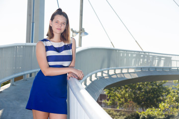 Girl in blue dress standing on city bridge