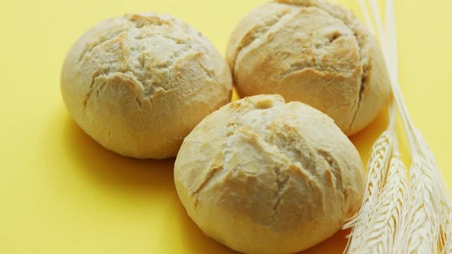 From above view of three round loafs of bread with wheat placed near on yellow background
