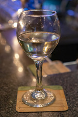 Half empty wine glass on a bar with a coaster under the stem.  Blurred background.