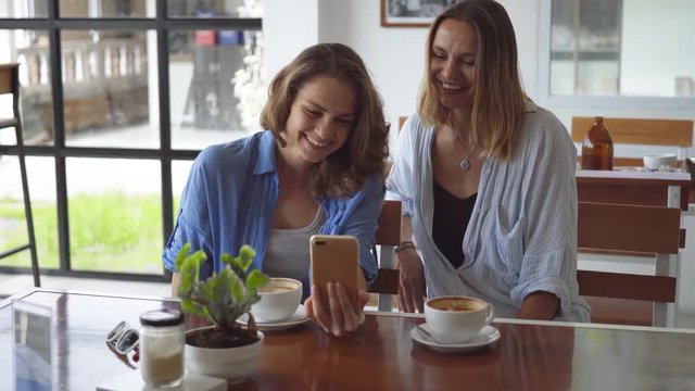 Two woman sharing coffee using smartphone in cafe