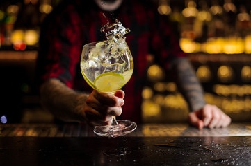Barman with tattoos holding a glass of fresh sour and sweet citrus cocktail