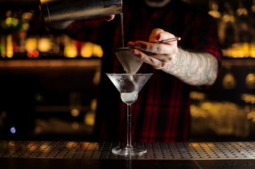 Barman pouring fresh and sour drink into a cocktail glass