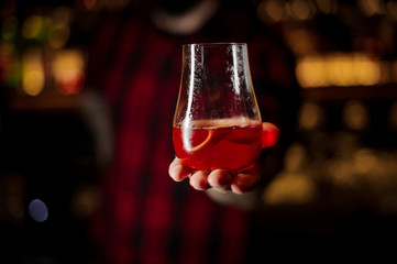 Barman holding a glass of fresh and sweet tasty red cocktail