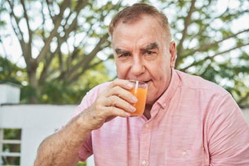 Positive healthy senior man drinking juice in outdoor cafe