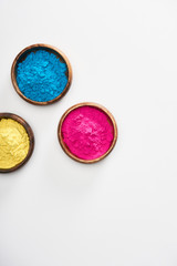 top view of wooden bowls with pink, blue and yellow holi powder on white background