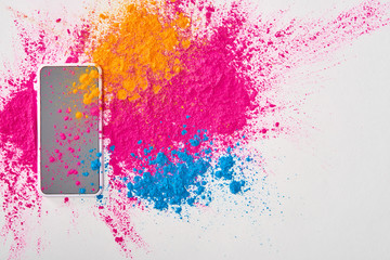 top view of smartphone and explosion of multicolored holi powder on white background