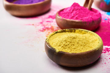 selective focus of wooden bowls with yellow, pink, blue and purple holi powder on white background