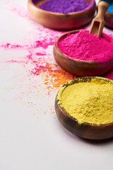 wooden bowls with pink and yellow holi powder on white background