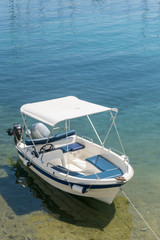 Obraz na płótnie Canvas Small white blue motorized boat anchored on the shore.