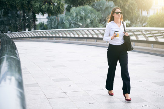 Serious successful female entrepreneur going to work with cup of take away coffee