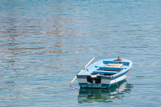 Small white blue boat with paddles anchored on the shore