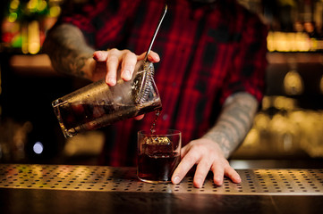 Barman pouring fresh strong alcoholic cocktail into a glass on bar