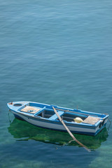 Fototapeta na wymiar Small white blue boat with paddles anchored on the shore