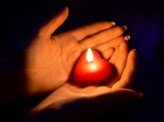 Women's hand holding a burning red candle in the dark