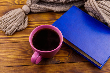 Cup of coffee, knitted scarf and book on wooden background