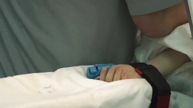 closeup little patient hand with pulsimeter fixed to lounge at operating process in modern surgery room