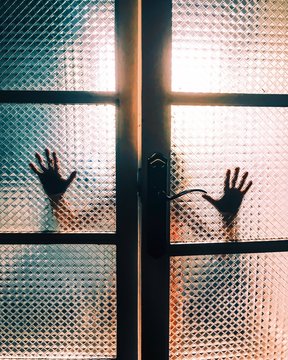 Backlit silhouette of hands touching a glass door