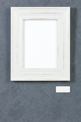 White wooden frame with blank caption tag on grey wall
