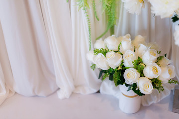 White roses in a vase with white drapery background.