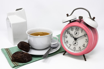 Traditional Italian breakfast with coffee and milk, cappuccino, and homemade chocolate biscuits. white ceramic cups on a white background. Vintage pink analog alarm clock. Wake up in the morning.