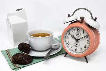 Traditional Italian breakfast with coffee and milk, cappuccino, and homemade chocolate biscuits. white ceramic cups on a white background. Vintage orange analog alarm clock. Wake up in the morning.