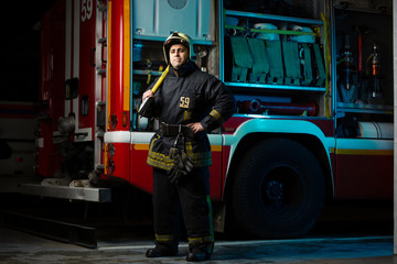 Full-length photo of firefighter man with pick near fire truck