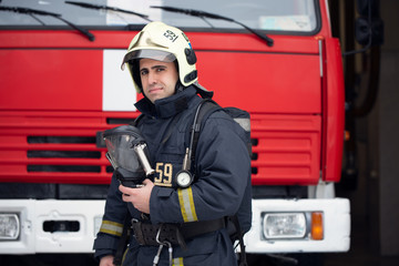 Image of man fireman with mask in hands near fire truck