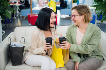 Two cute girl walks in the Mall with gift bags. Happy and smiling after shopping with a lot of purchases